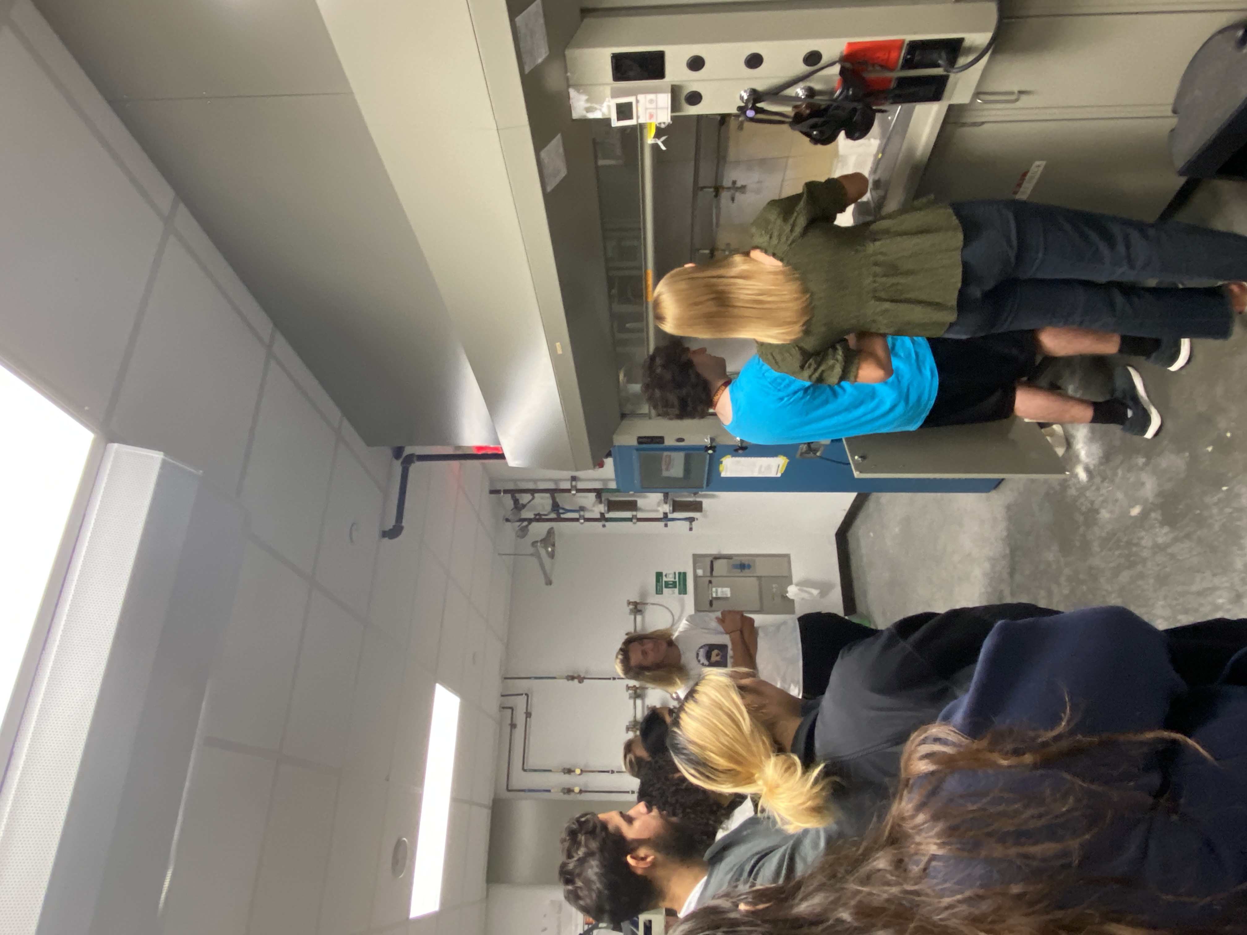 Students watch an experiment under a lab hood